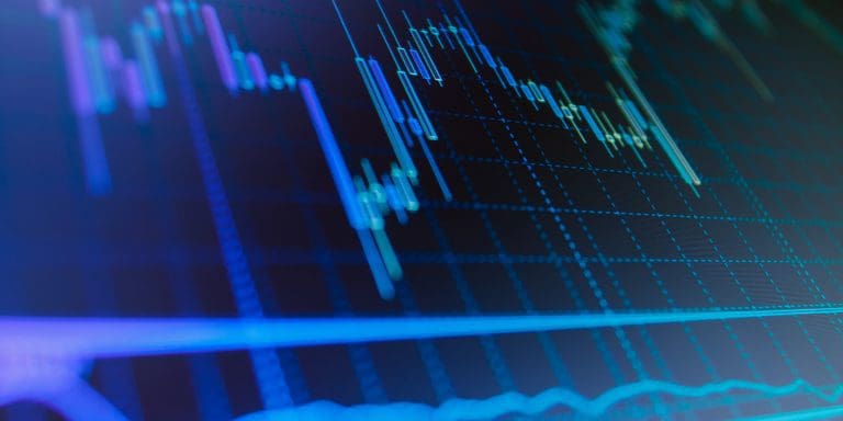 Close-up of a candlestick stock chart on a digital screen with blue and green trend lines and grid overlay.
