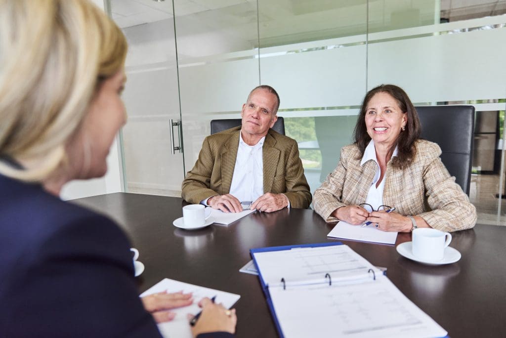 Financial advisor meeting with a mature couple across a conference table, reviewing documents and a binder.